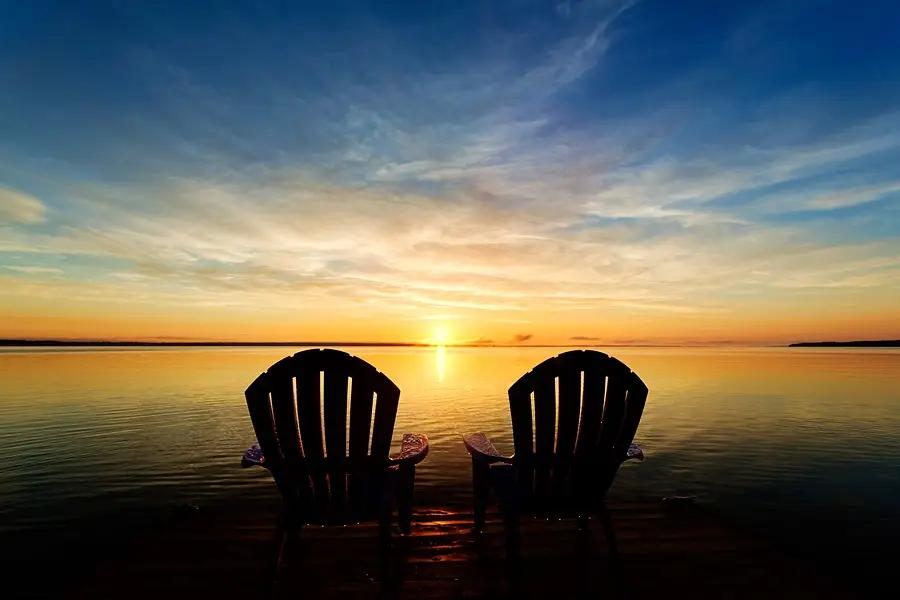 Two empty Adirondack chairs facing a calm lake at sunset, symbolizing peace and hope in recovery.