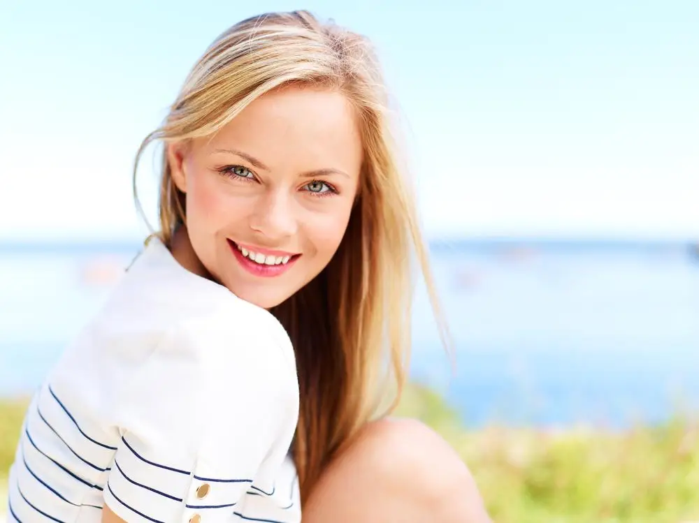Smiling young woman outdoors by the water, looking hopeful and at peace during addiction recovery.