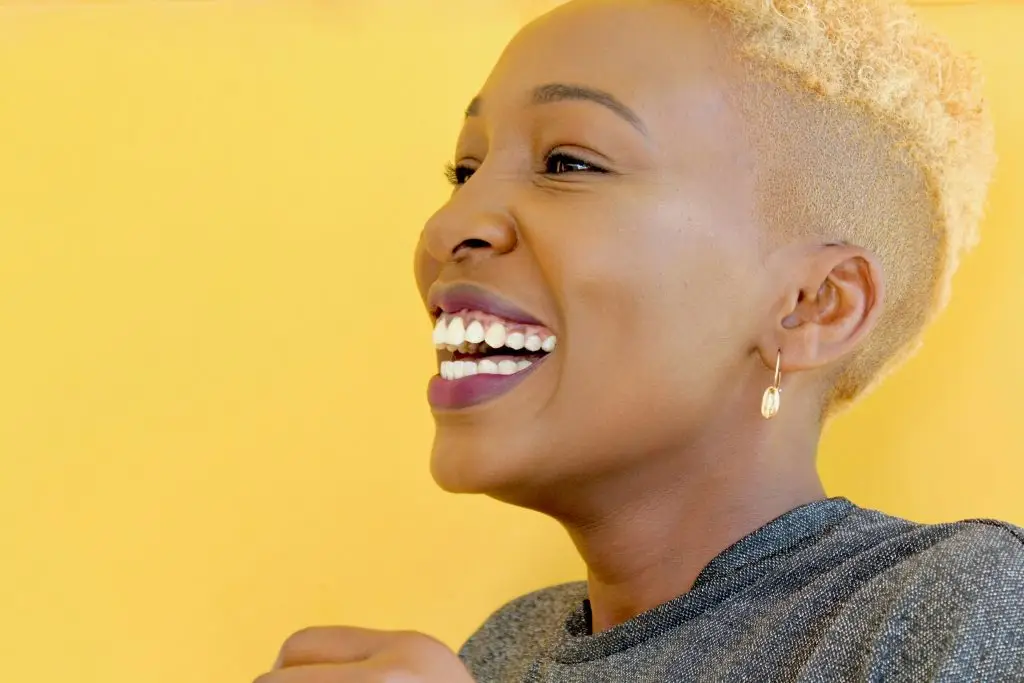 Woman with short blonde hair smiling joyfully against a bright yellow background.