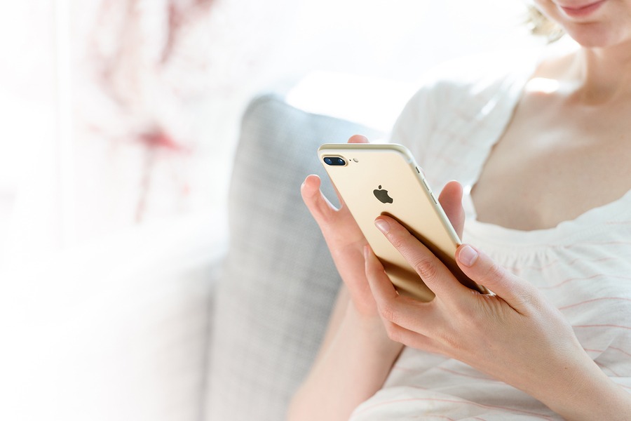 Woman holding a gold smartphone while sitting on a couch, reaching out for help or support.