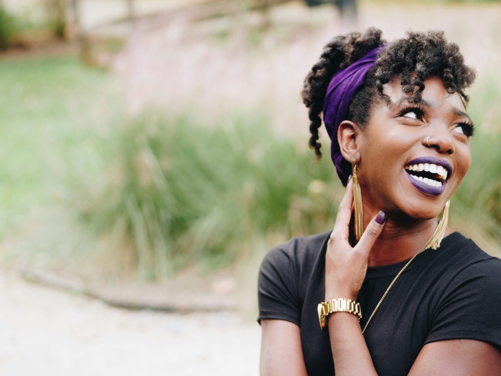 Woman with a purple headband laughs joyfully outdoors, radiating hope and confidence in a sunlit natural setting.