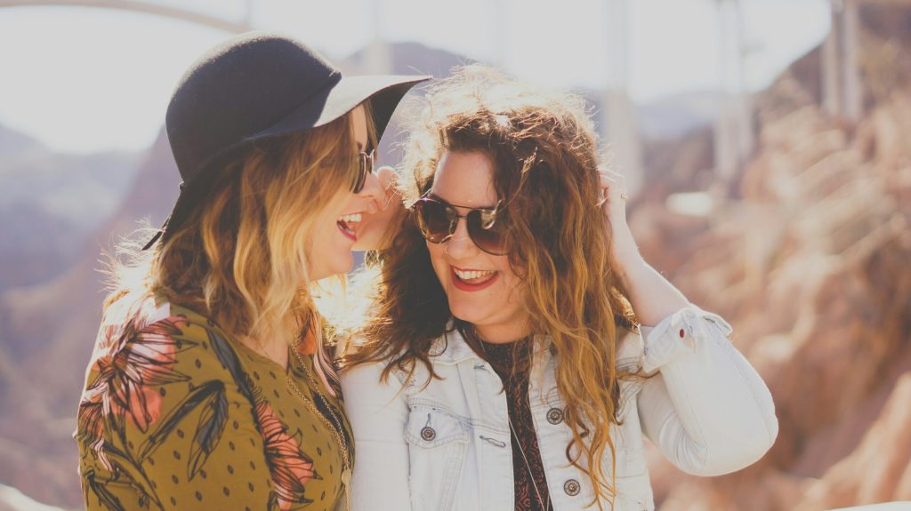 Two women laughing together outdoors in sunlight, sharing a joyful moment of friendship and support.