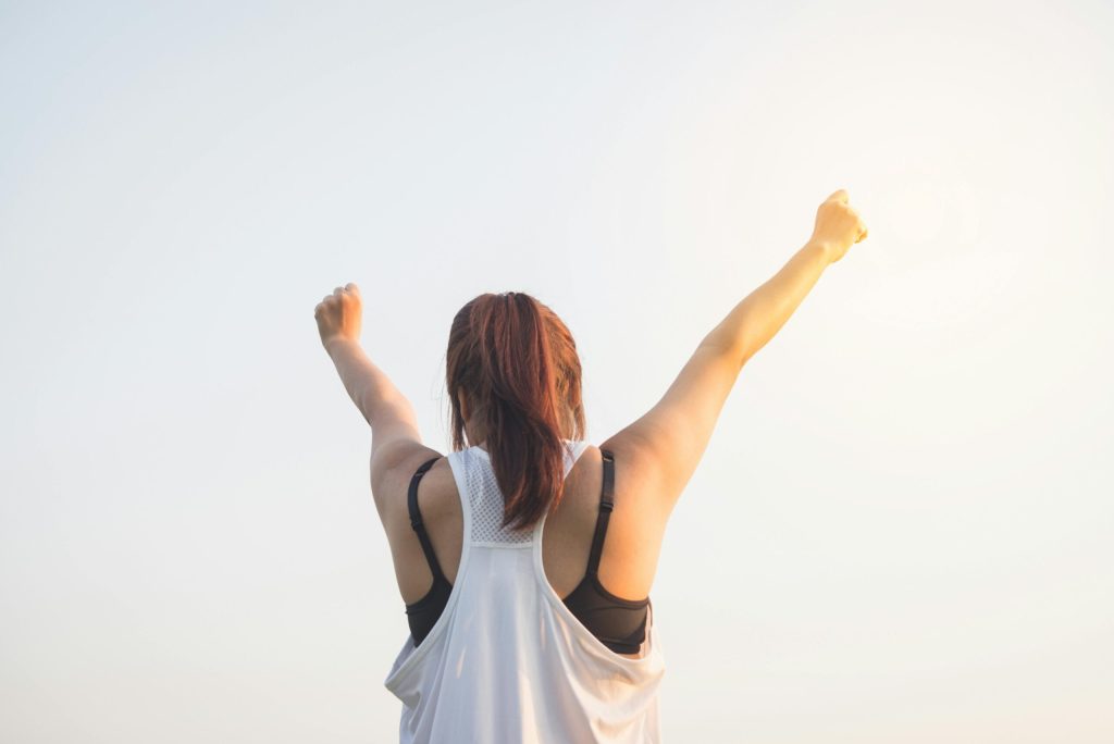 Woman raising both fists triumphantly against a bright sky, celebrating strength and recovery.